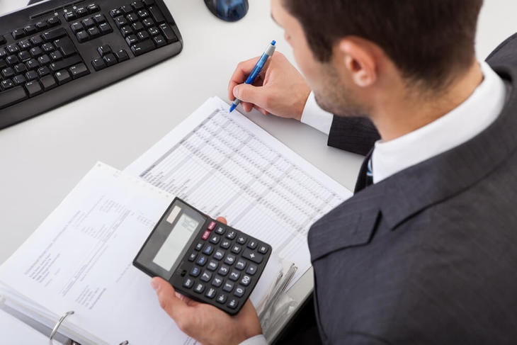 Homem segurando calculadora enquanto analisa dados contábeis