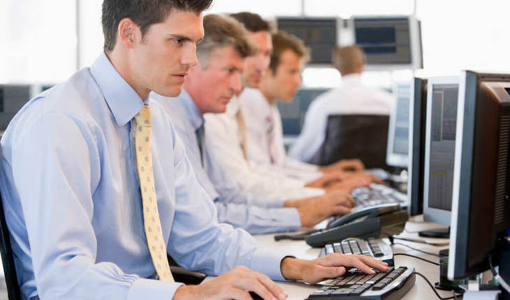 Pessoas com trajes sociais numa sala de escritório utilizando computador