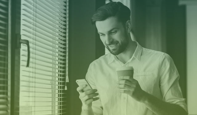 Homem utilizando celular com um copo de café na mão