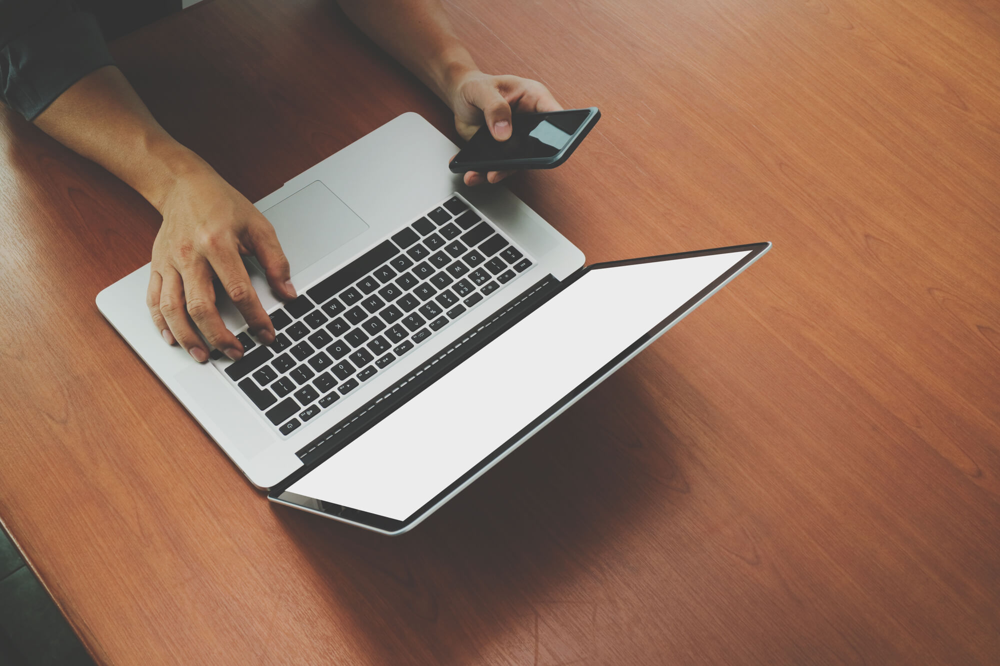 Pessoa usando um celular e um laptop sobre uma mesa