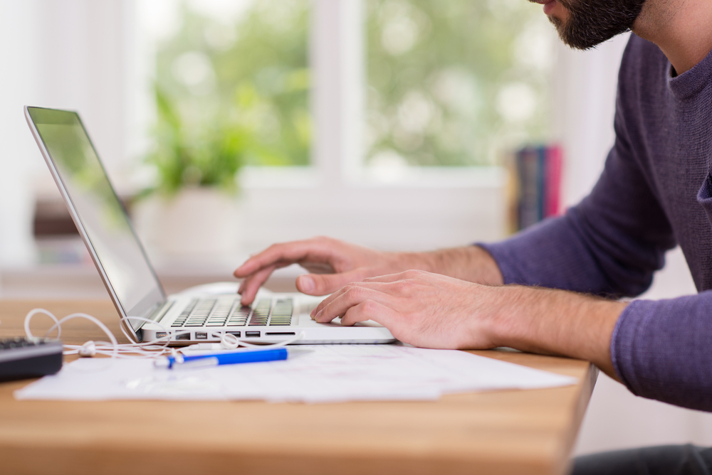 Homem utilizando computador com papel e caneta