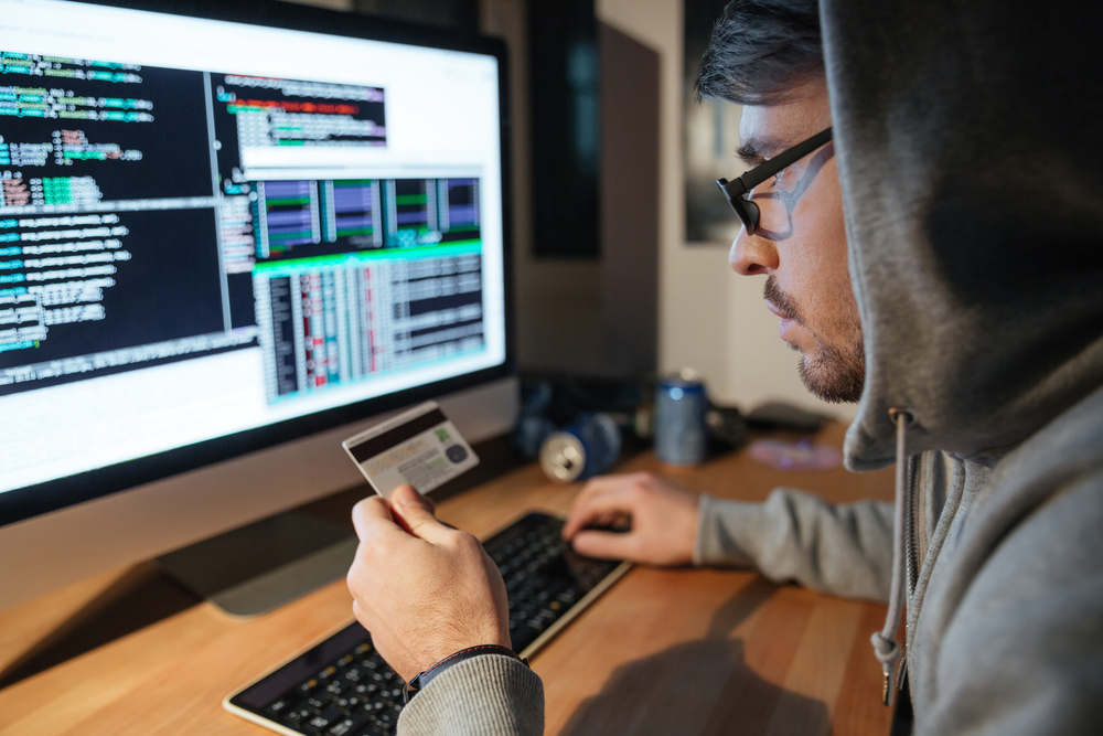 Homem segurando cartão utilizando computador com tela exibindo códigos