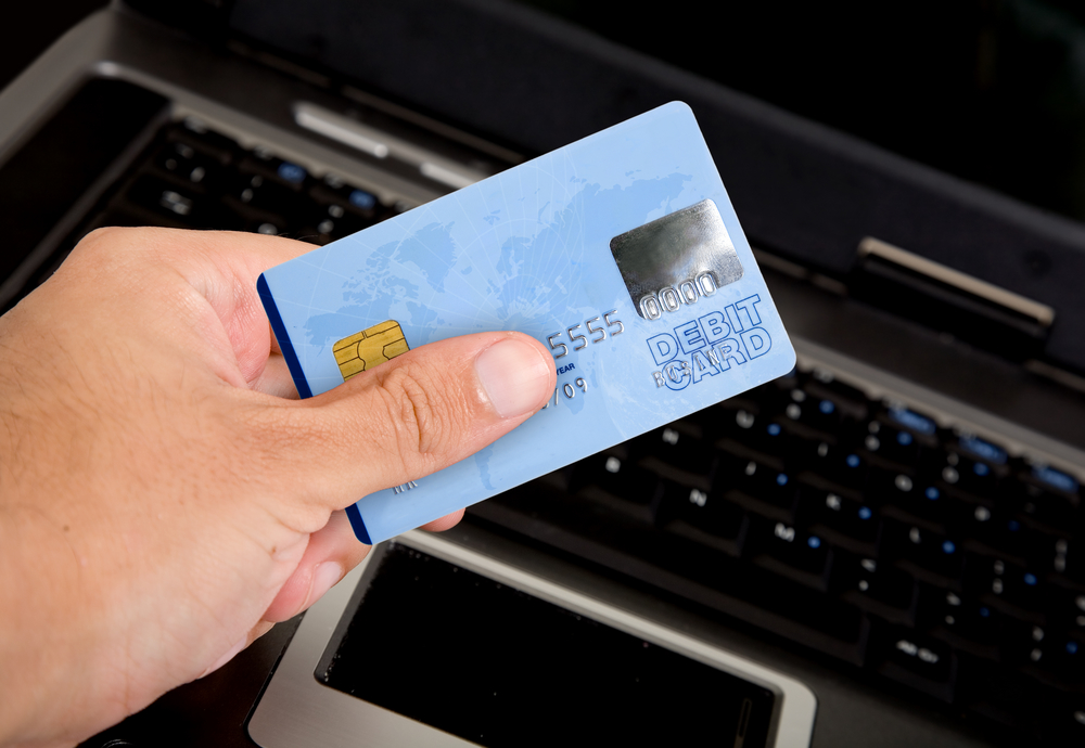 Homem segurando cartão de crédito com computador ao fundo