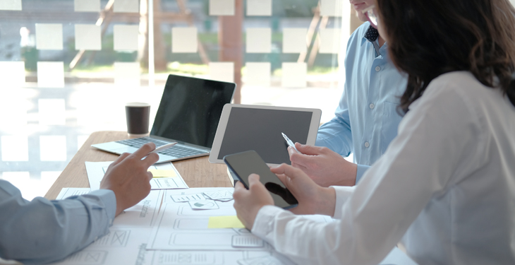 Pessoas em uma mesa de reunião utilizando dispositivos móveis e papel