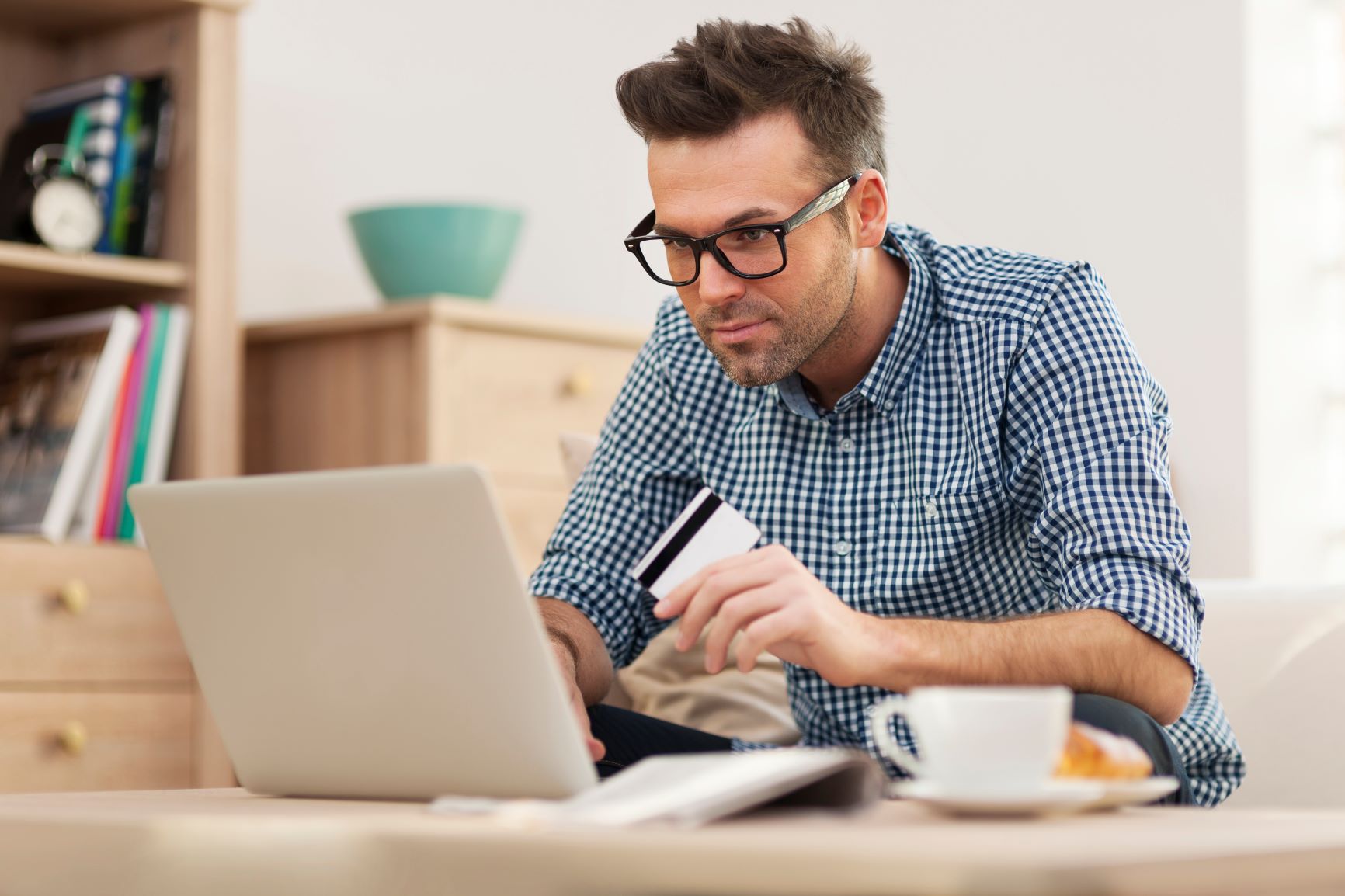 Homem com cartão na mão utilizando um computador e tomando café