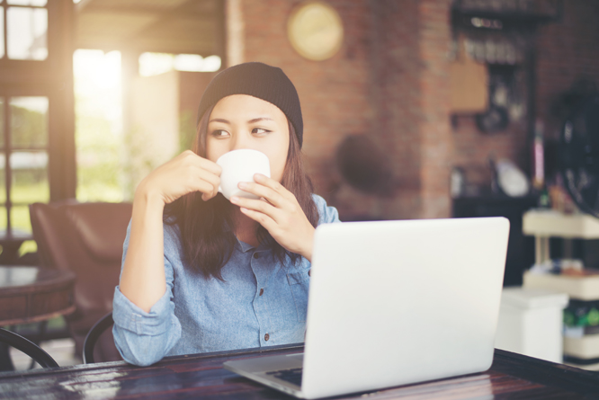 Mulher tomando café em xícara enquanto utiliza computador em cafeteria