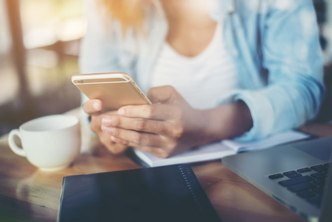 Mulher utilizando celular com computador em cima da mesa