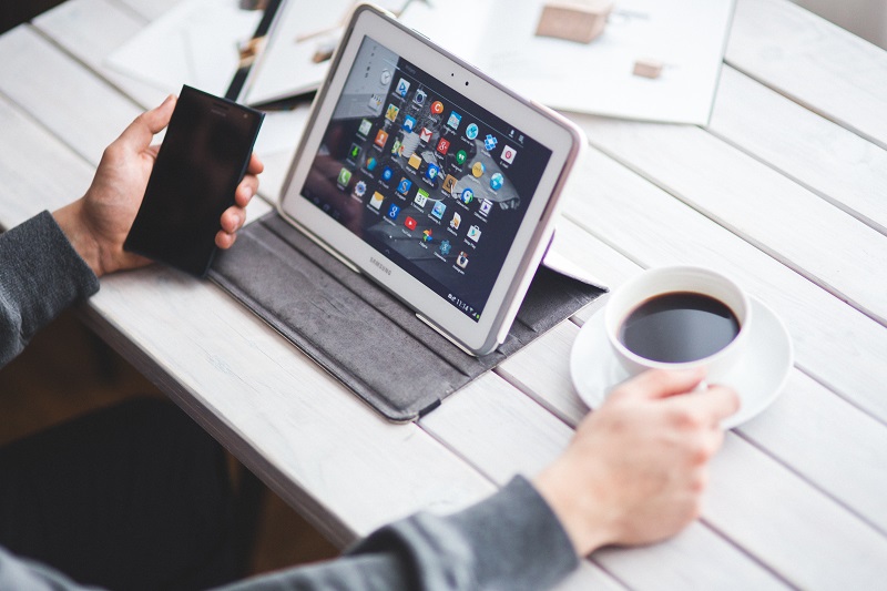 Pessoa vendo seu tablet samsung enquanto toma café