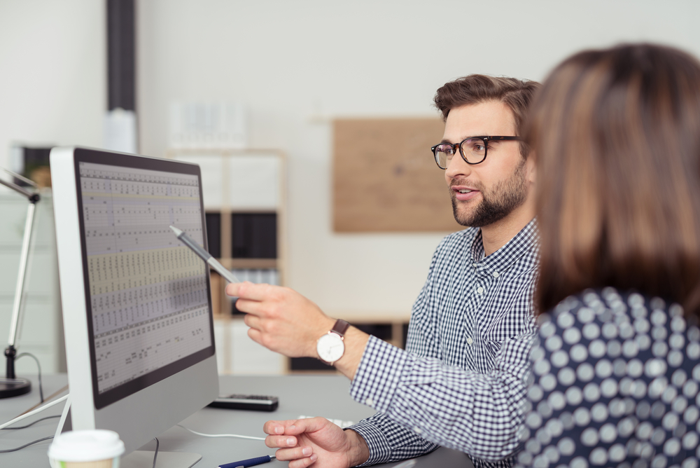 Homem analisando dados na tela de um computador enquanto conversa com mulher