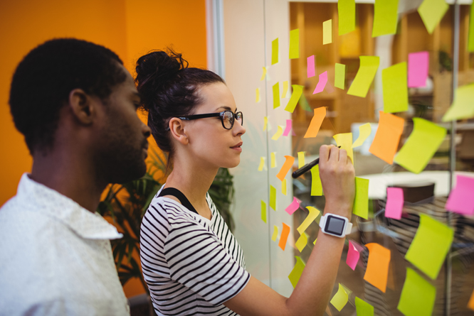 Pessoas escrevendo em post-its colados em mural