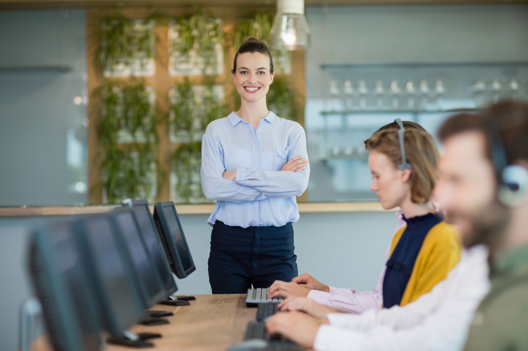 Mulher com trajes sociais sorrindo enquanto atendentes utilizam o computador