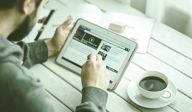 Homem tomando xícara de café enquanto lê um canal de notícias em tablet