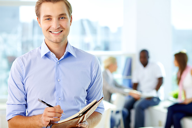 Homem sorrindo de camisa social segurando um caderno