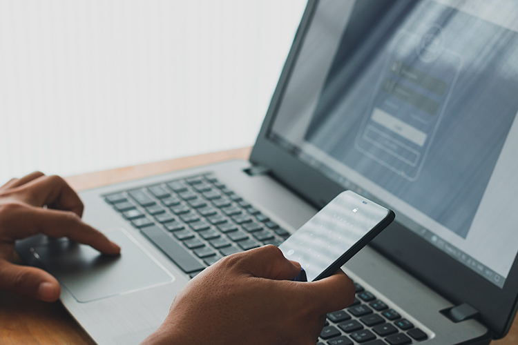 Homem utilizando o computador com celular na mão fazendo verificação de segurança