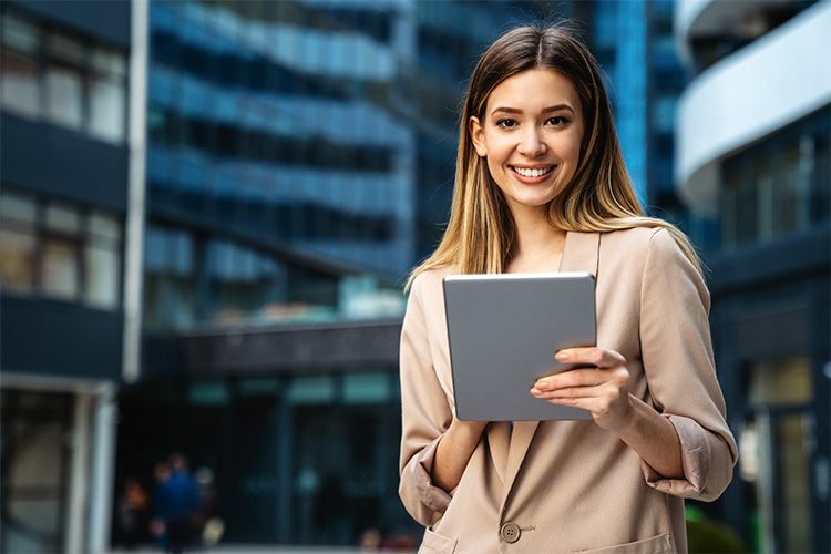 Retrato de uma mulher de negócios bem-sucedida usando tablet digital em frente a um prédio de negócios moderno.